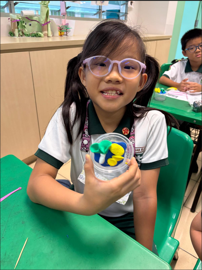 Student proudly showing a handmade lantern craft during a classroom art activity, with classmates working on similar projects in the background